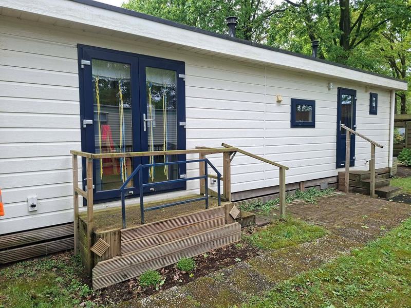 Zijkant van het chalet met houten veranda en trapje naar de voordeur